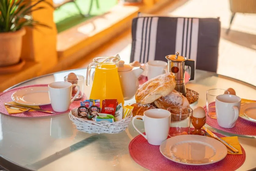 A breakfast table with cups, pastries, juice, and a coffee press.
