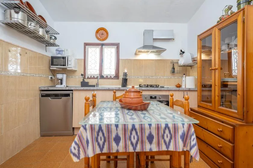 A tiled kitchen with a patterned tablecloth-covered dining table in the center.