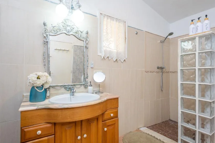 A bathroom with a wooden vanity, ornate mirror, and shower.