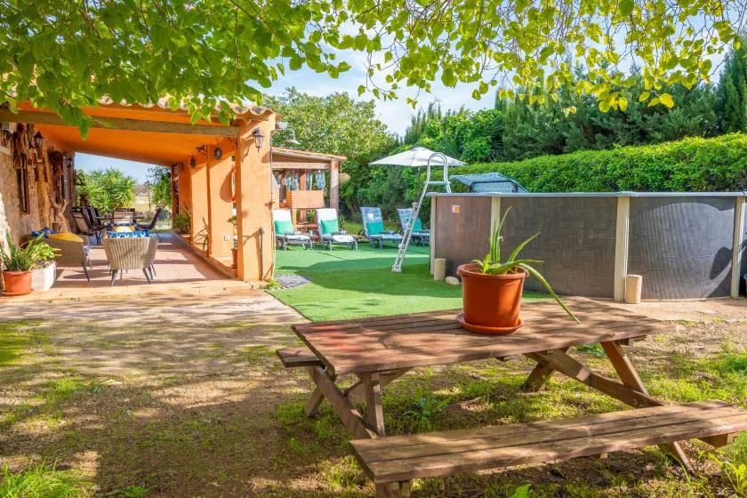 A shaded outdoor patio and garden with seating, greenery, and a picnic table.