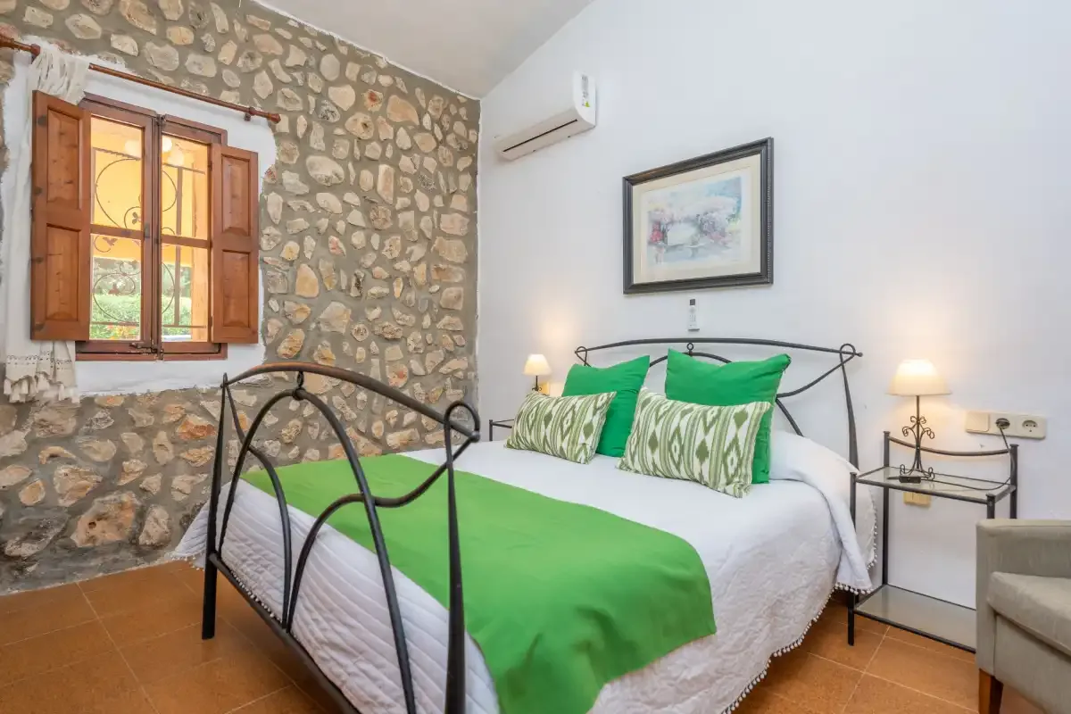 A bedroom with a bed dressed in green and white beside a stone wall.