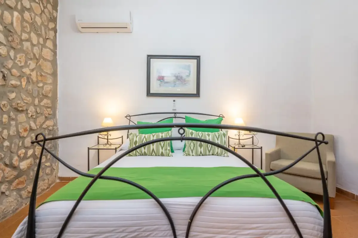 A bedroom with a green bedspread, bedside tables, and framed wall art.