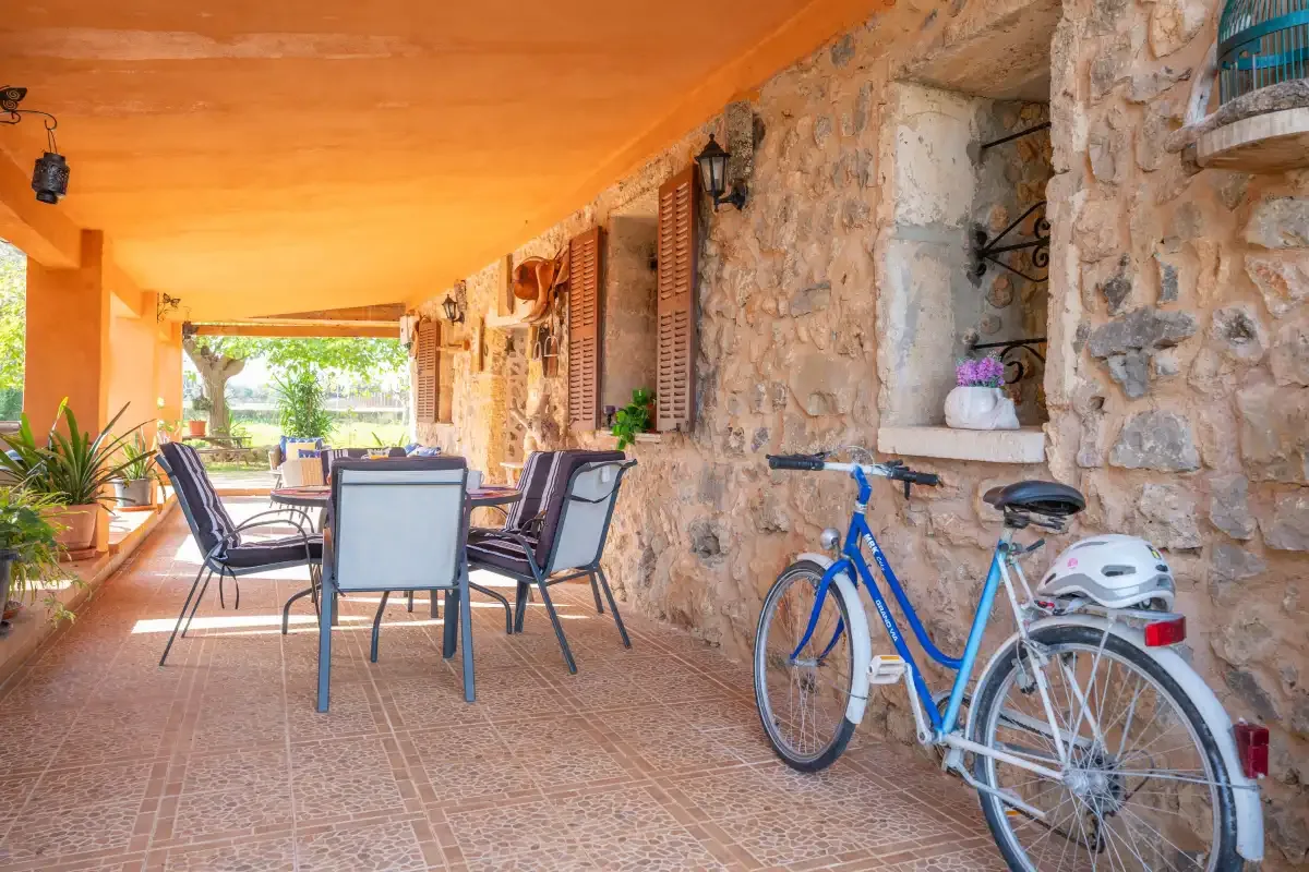 A covered patio with outdoor seating and a bicycle beside a stone wall.