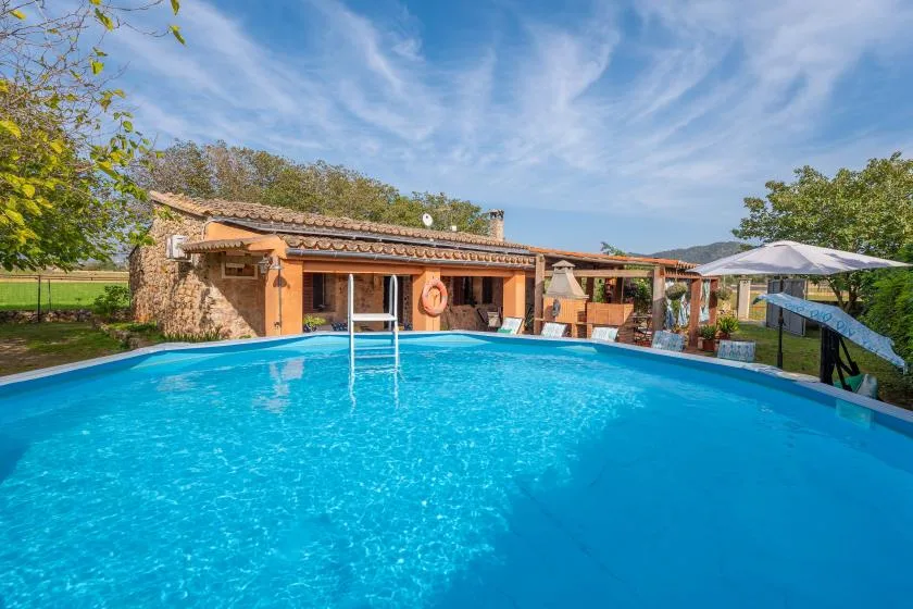 An outdoor swimming pool in front of a rustic building and covered patio.