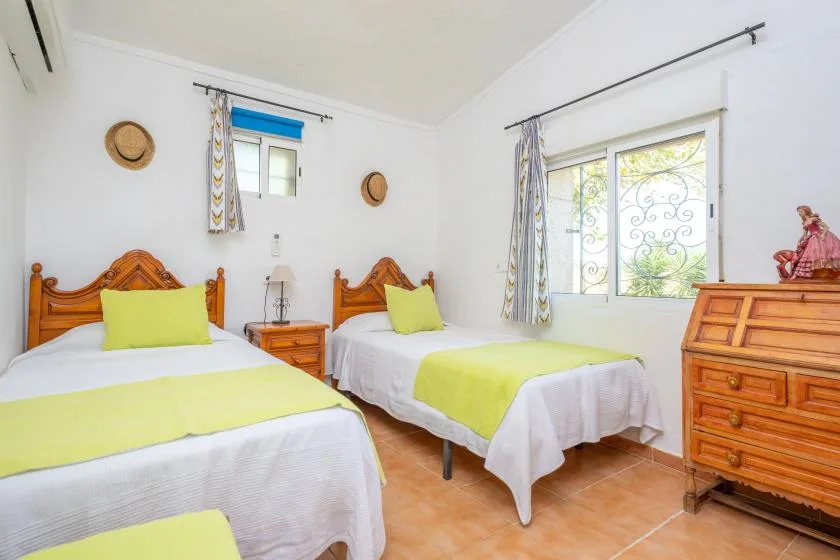 A bright bedroom with two beds dressed in white and lime-green linens.