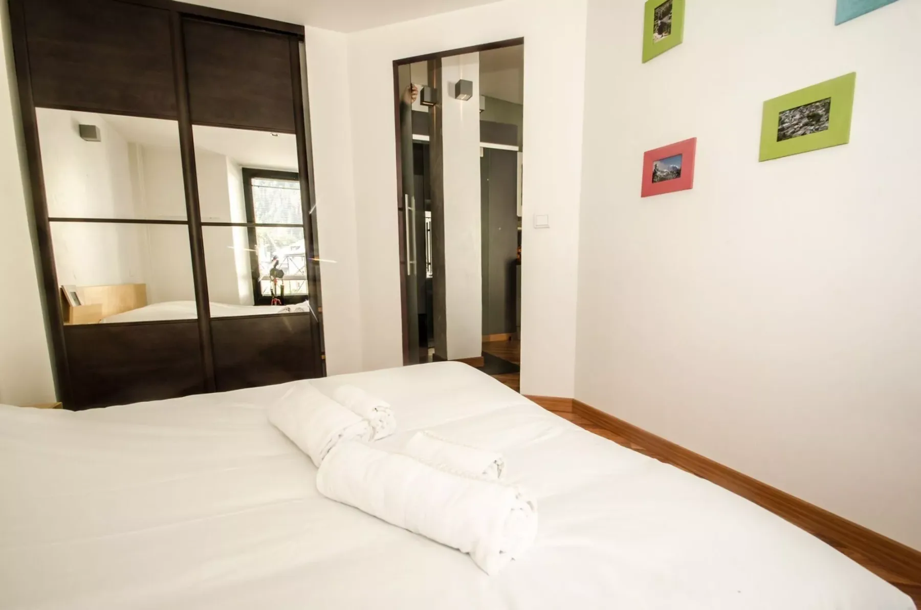 A bedroom with white bedding and dark-framed mirrored closet doors.