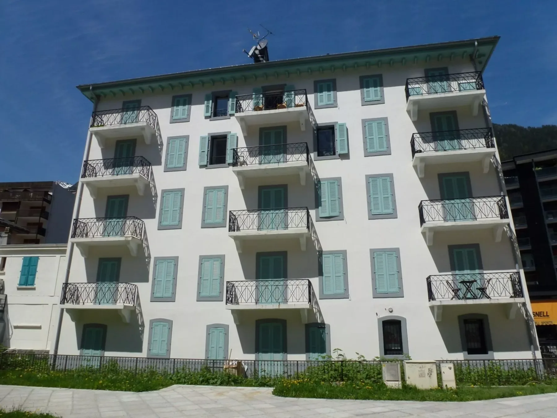 Un edificio de varias plantas con contraventanas verde claro y balcones salientes.
