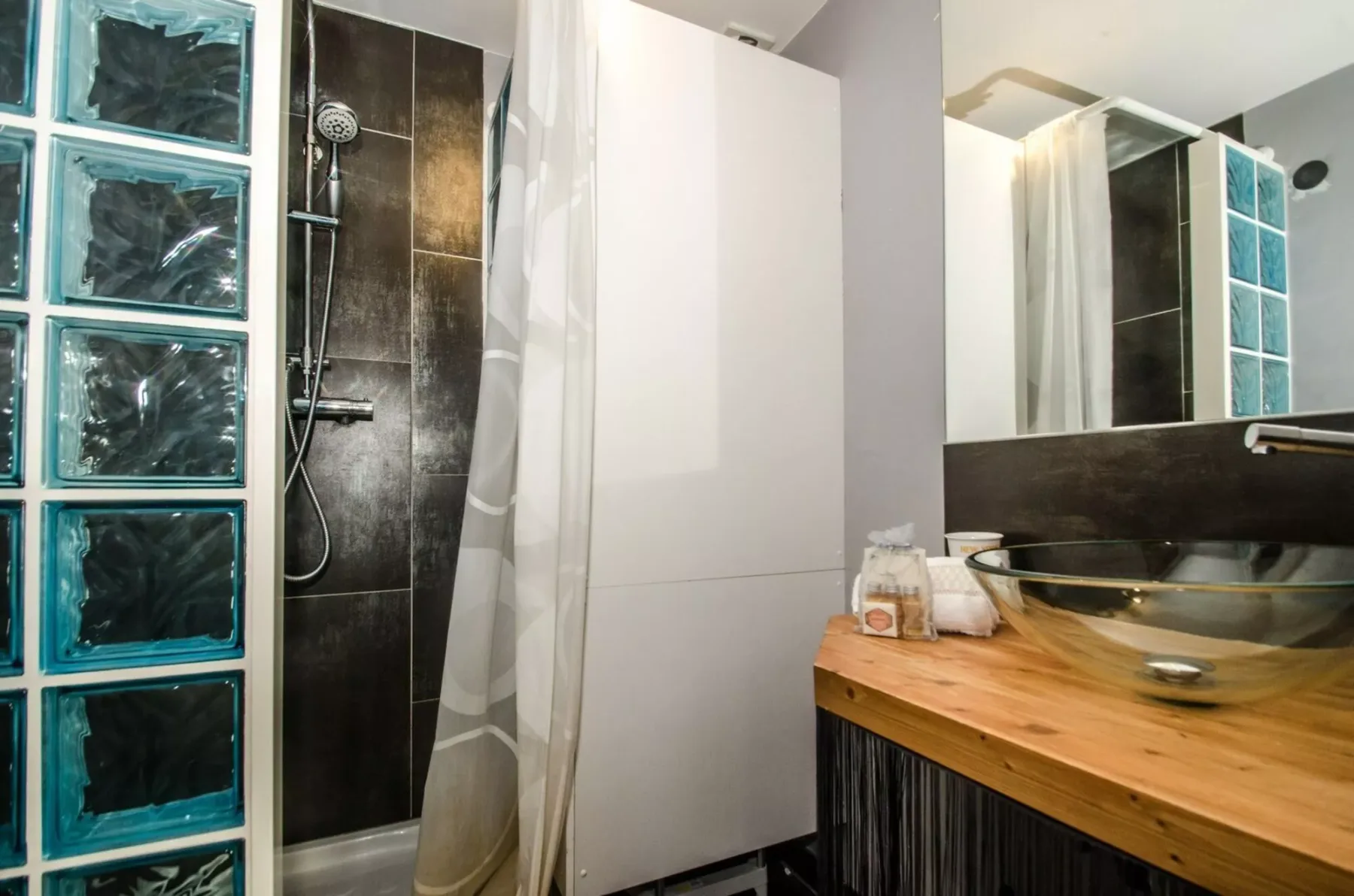 Un baño con una pared de bloques de vidrio, ducha y tocador de madera.