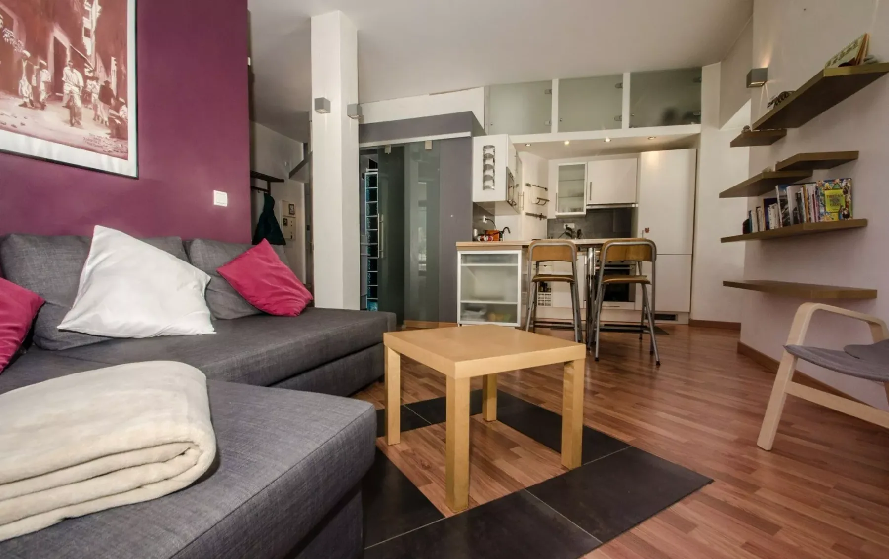 Una zona de estar con asientos grises y una mesa de centro de madera junto a una cocina compacta.