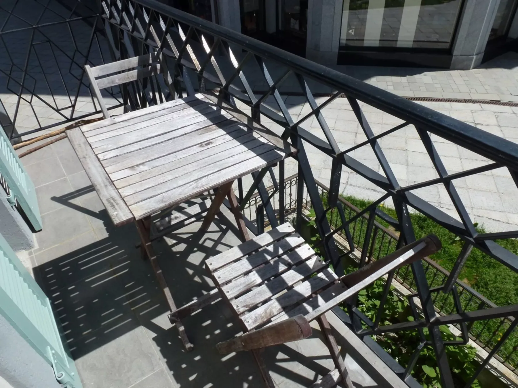 Un pequeño patio exterior con asientos de madera junto a una barandilla metálica negra.
