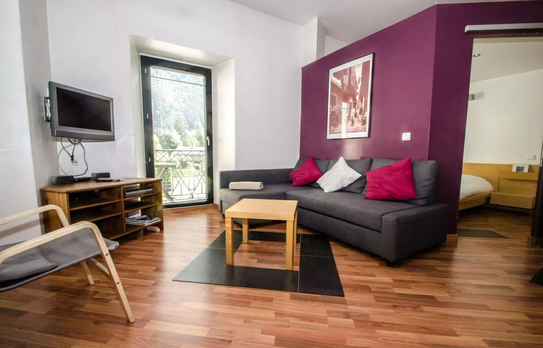 Una sala de estar con un sofá seccional oscuro, una mesa de centro y un televisor en la pared.