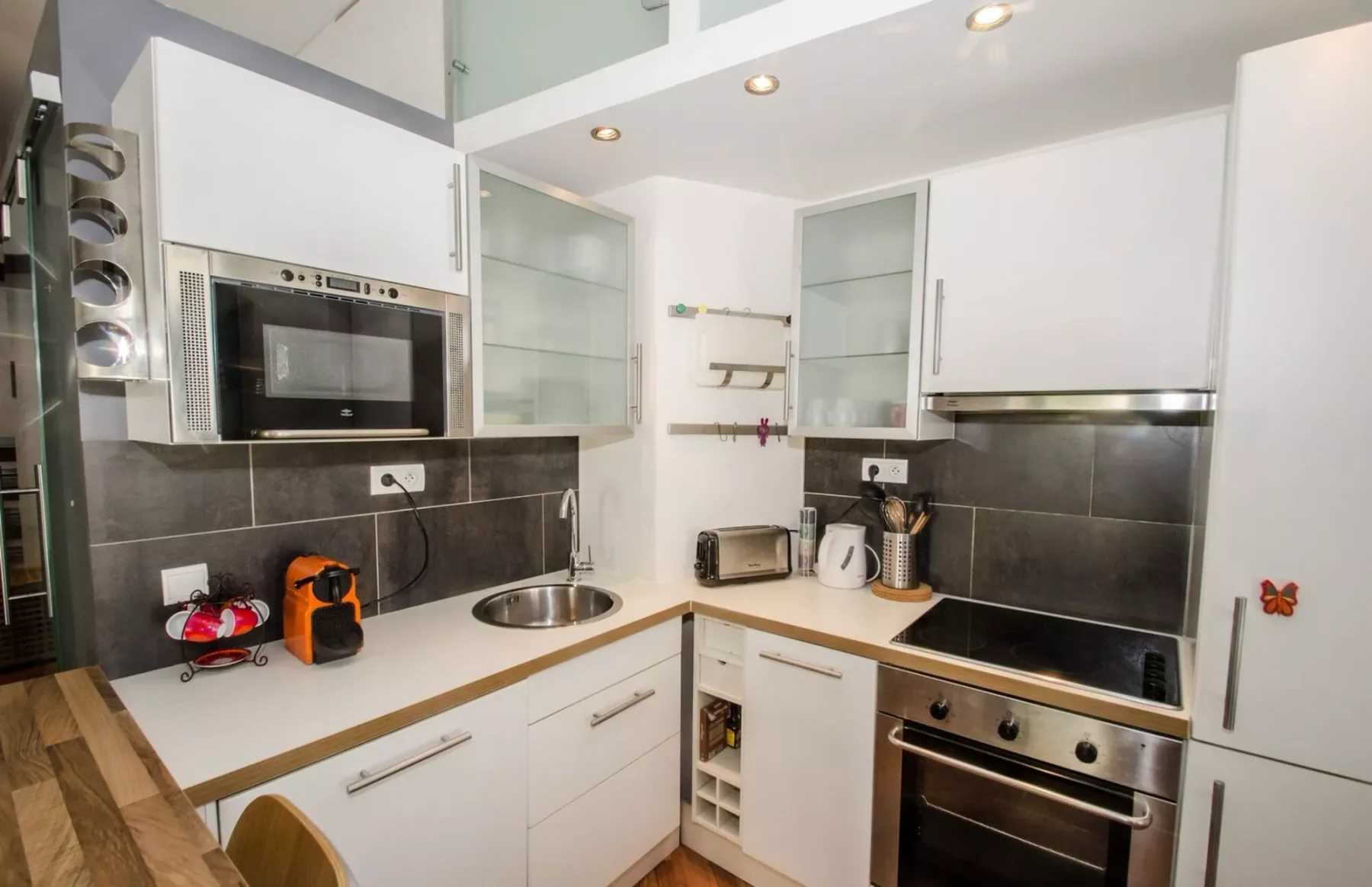 A modern white kitchen with dark backsplash, built-in appliances, and a countertop sink.