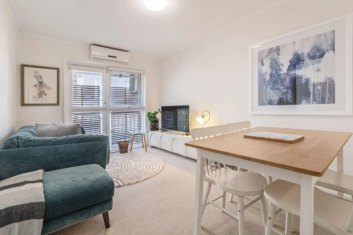 A bright living and dining area with a teal sectional, table, and large windows.