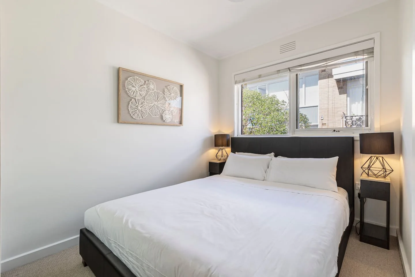 Dormitorio con una cama bien arreglada, mesas de noche y una ventana amplia.