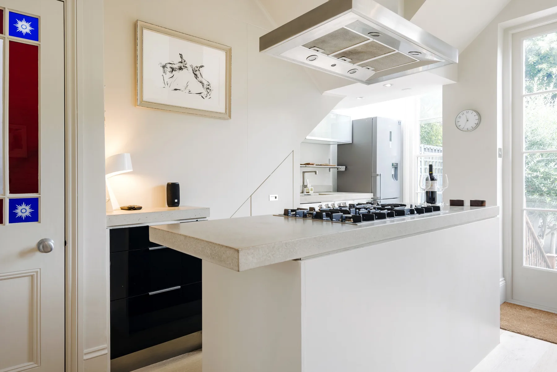 A bright kitchen with a central island, cooktop, and stainless steel range hood.