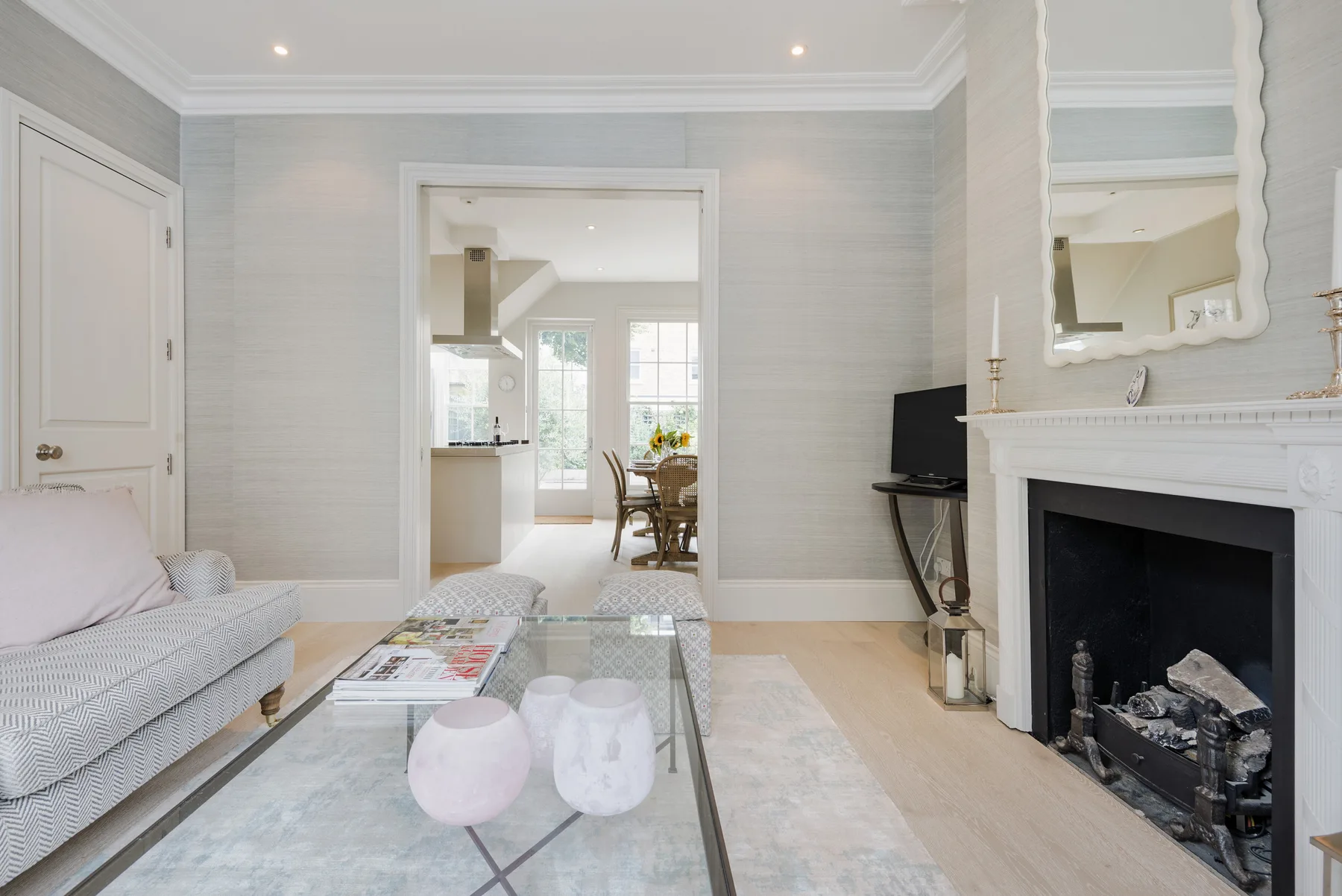 A bright living room with seating, a glass coffee table, and a fireplace.