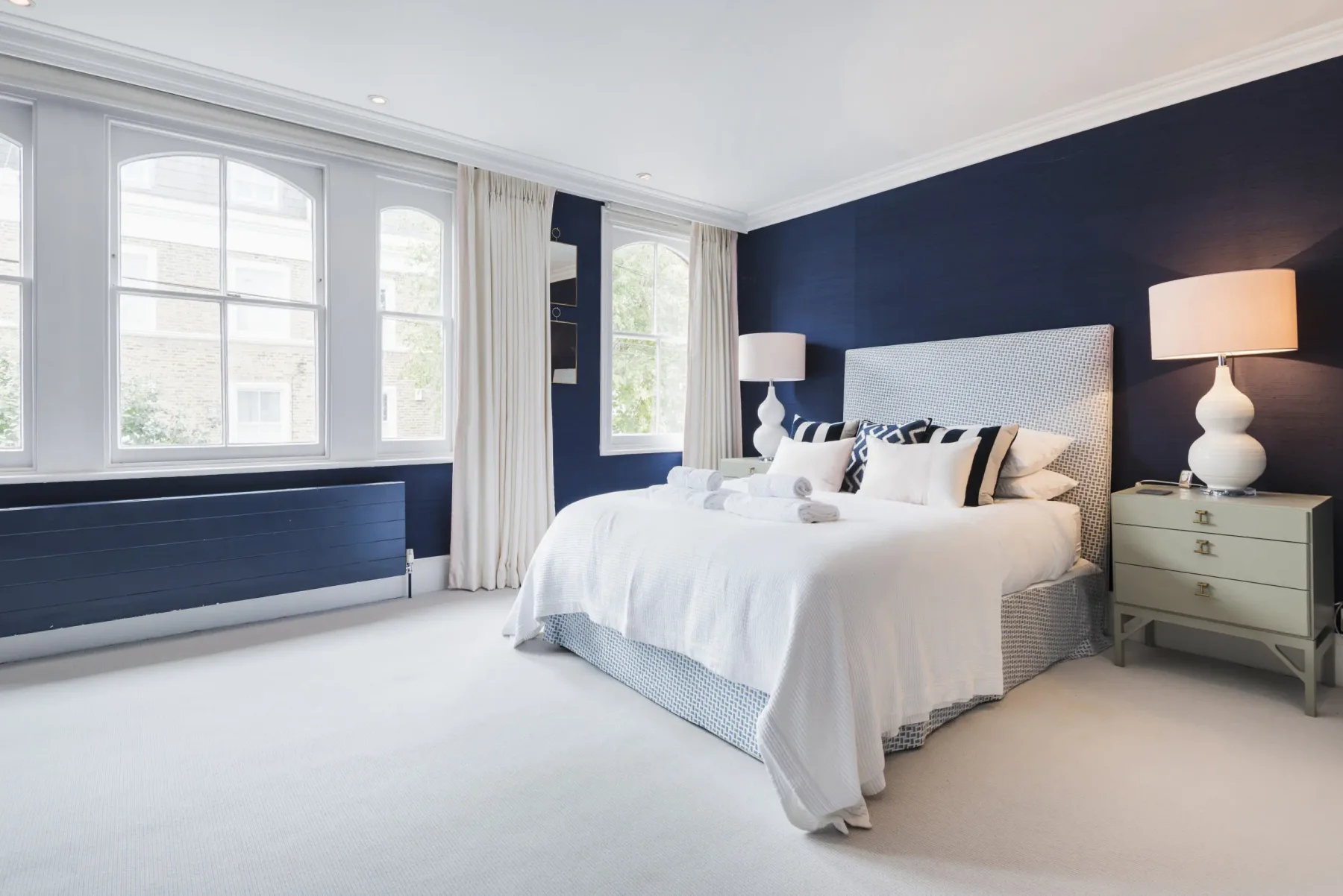 A bedroom with a bed, bedside tables, and tall windows.