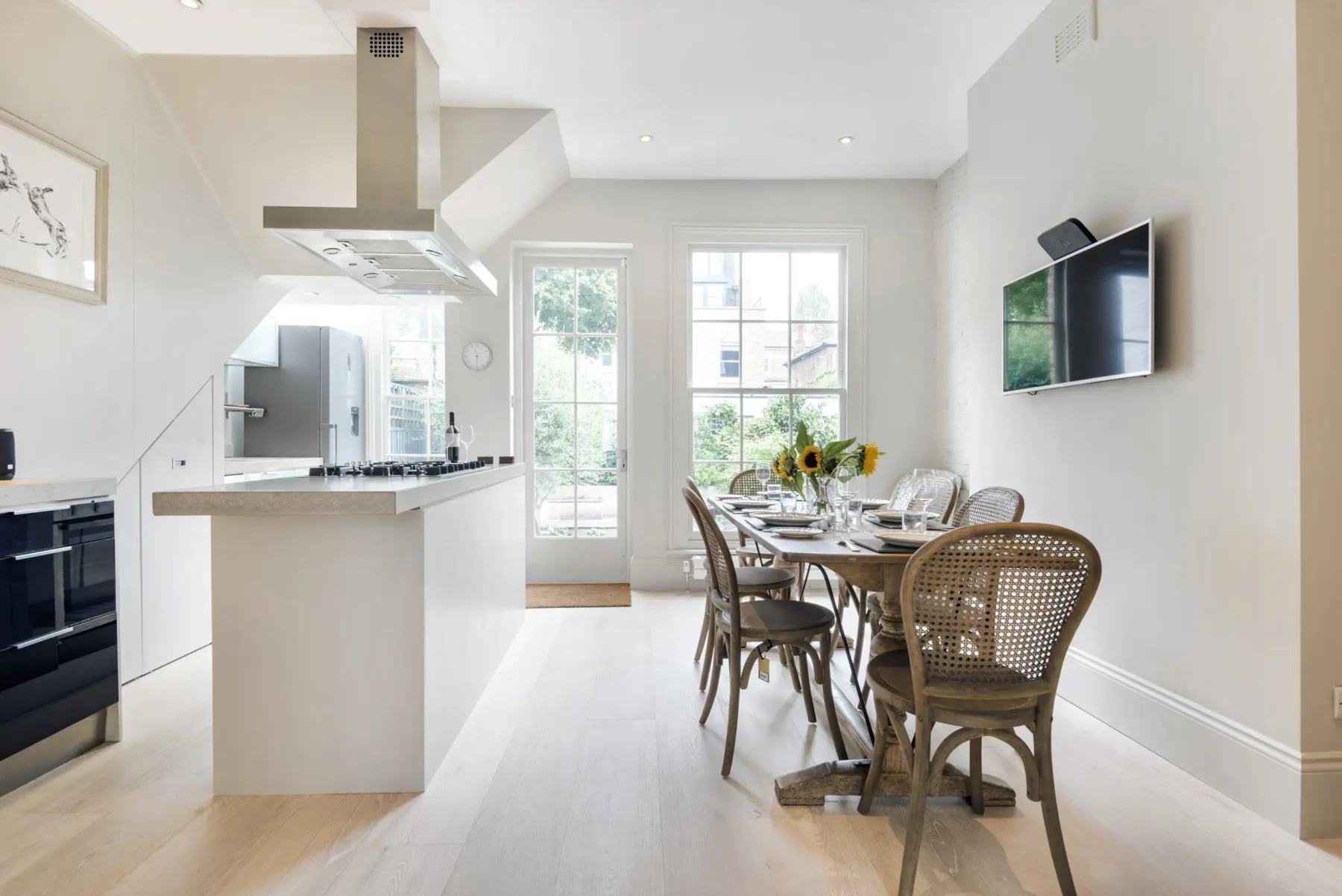 An open-plan kitchen and dining area with a table beside tall windows.