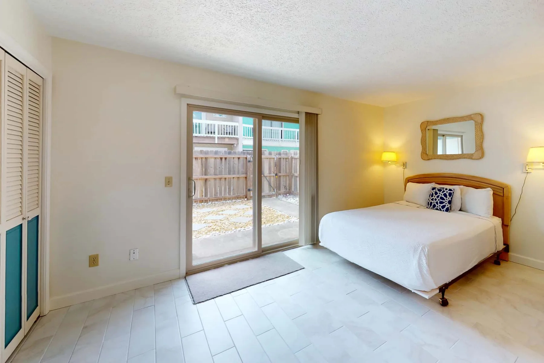 A bedroom with a bed and sliding glass doors opening to a fenced yard.