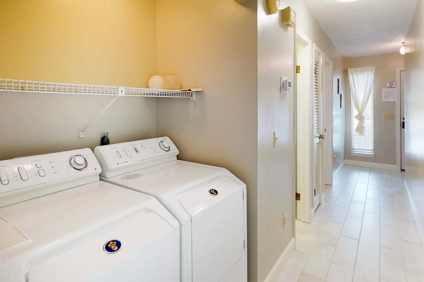 A laundry area with two white machines beside a tiled hallway.