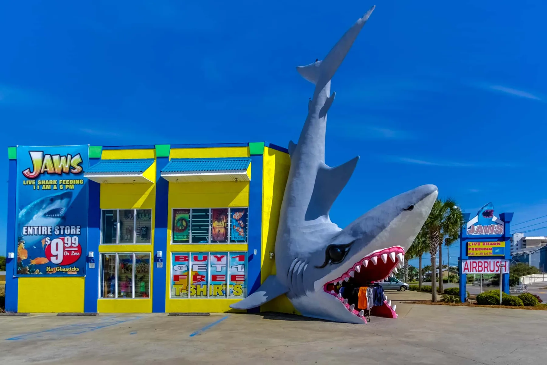 A bright yellow storefront stands beside a large shark-shaped roadside display.