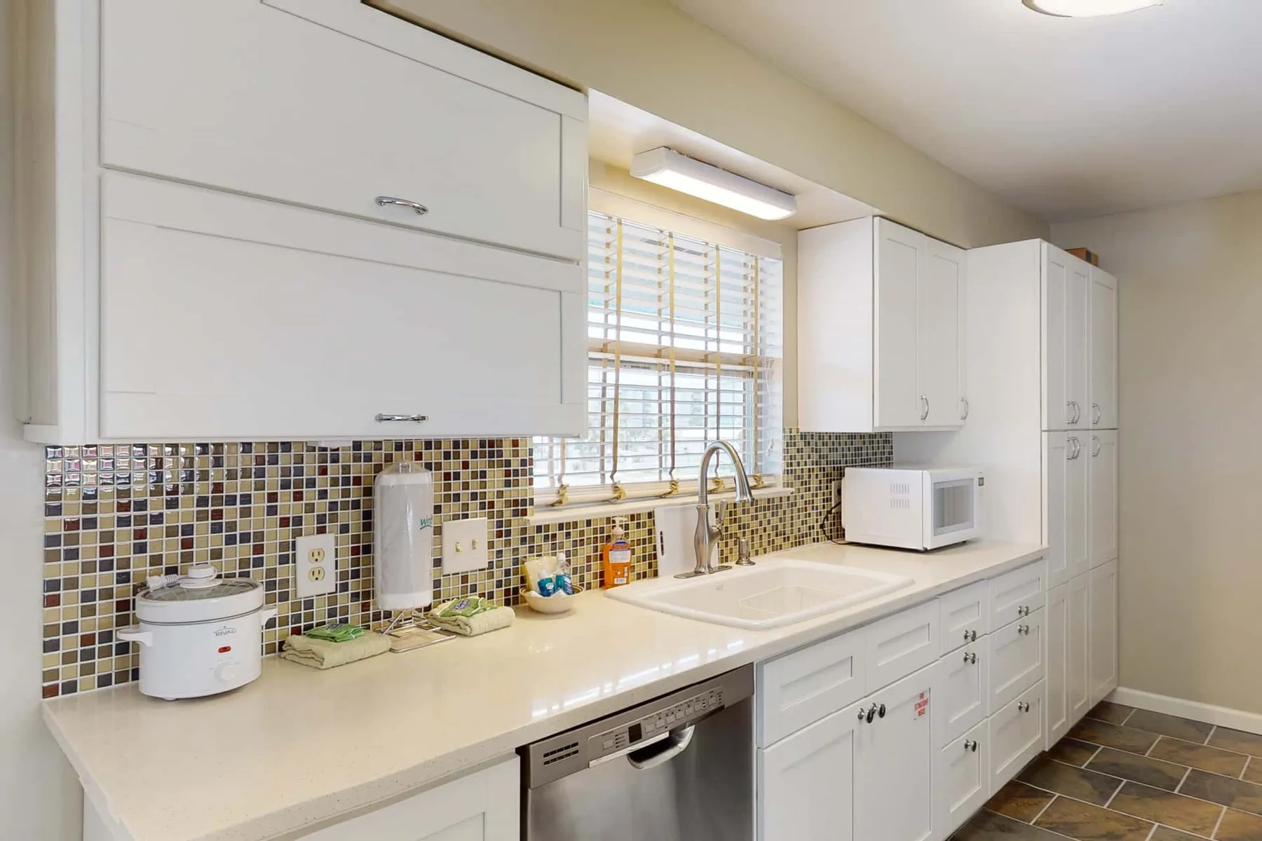 A bright kitchen with white cabinets, a long counter, and a window above the sink.