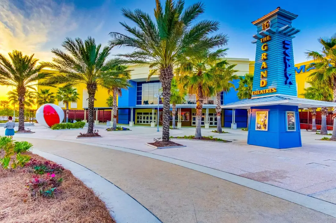 A theater entrance and a tall sign stand among palm trees beside a paved walkway.