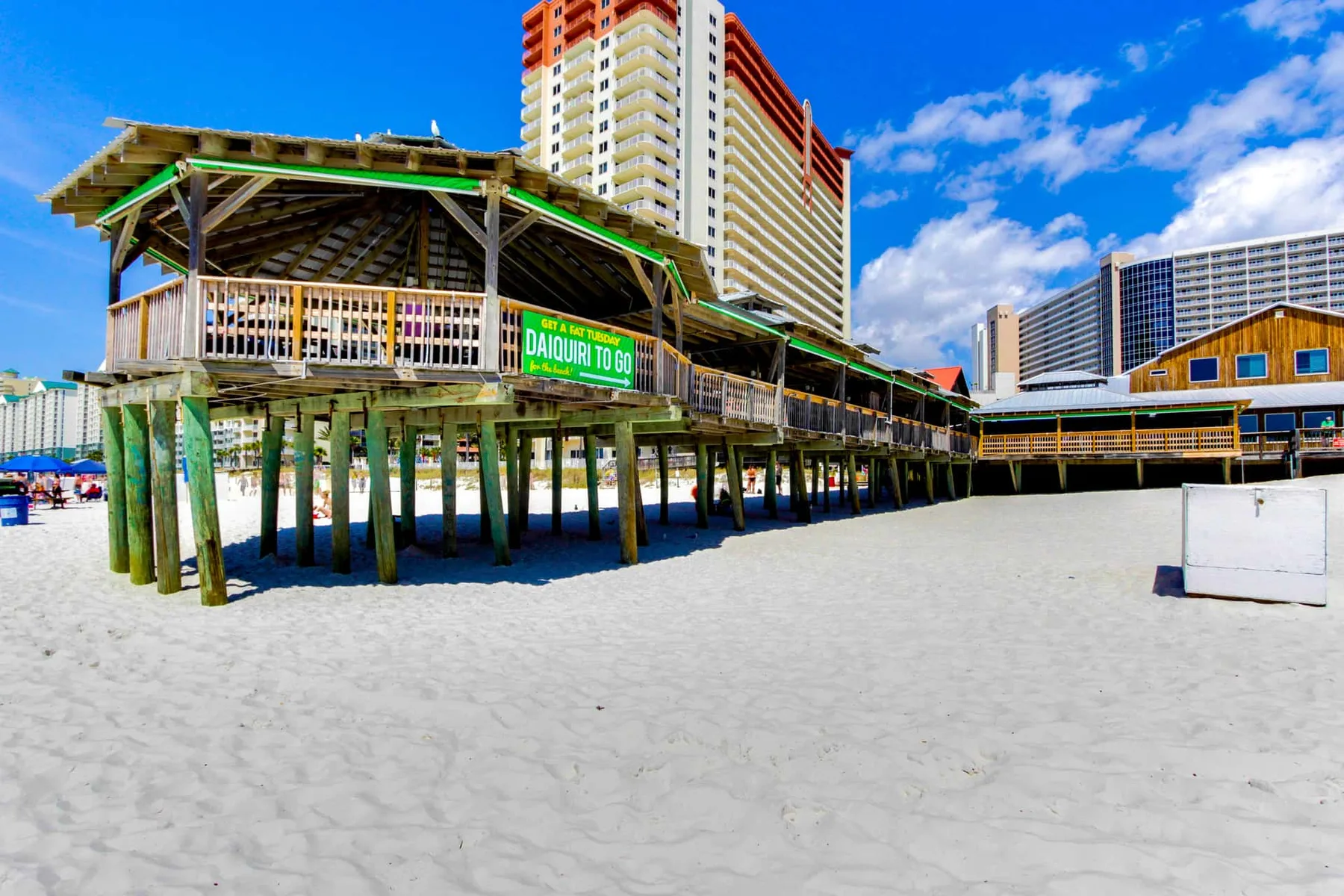 A raised boardwalk extends over a sandy beach beneath a bright blue sky.