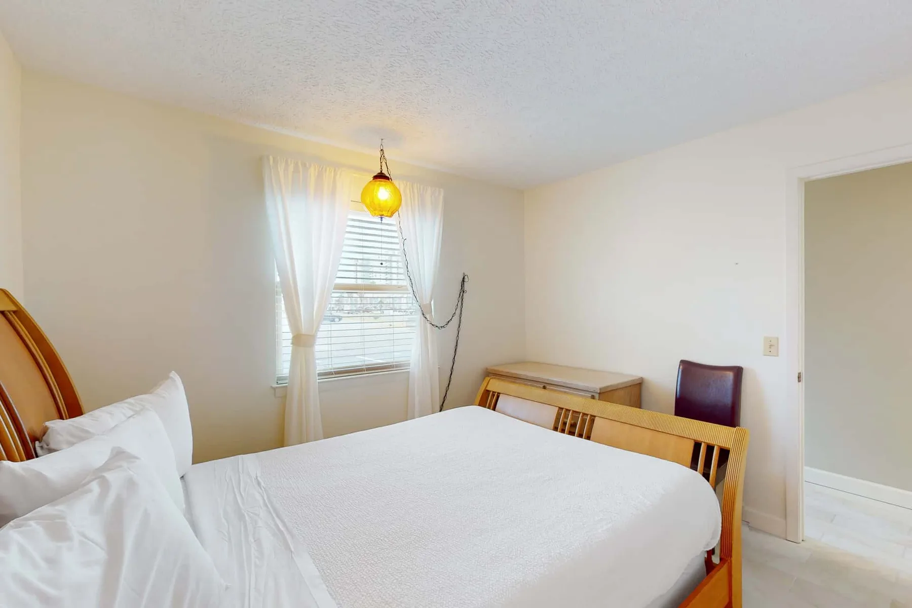 A bedroom with a bed beneath a window dressed with sheer curtains.