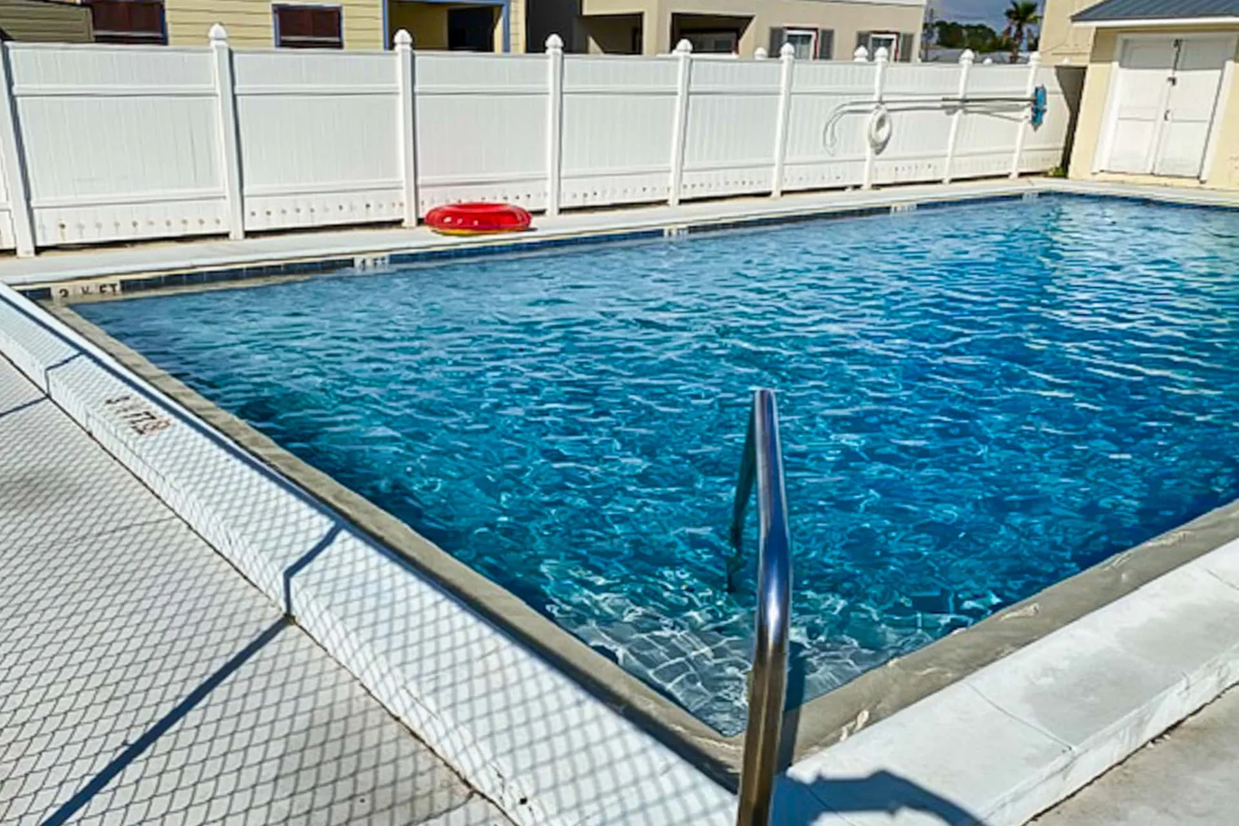 An outdoor swimming pool with blue water and a metal handrail.