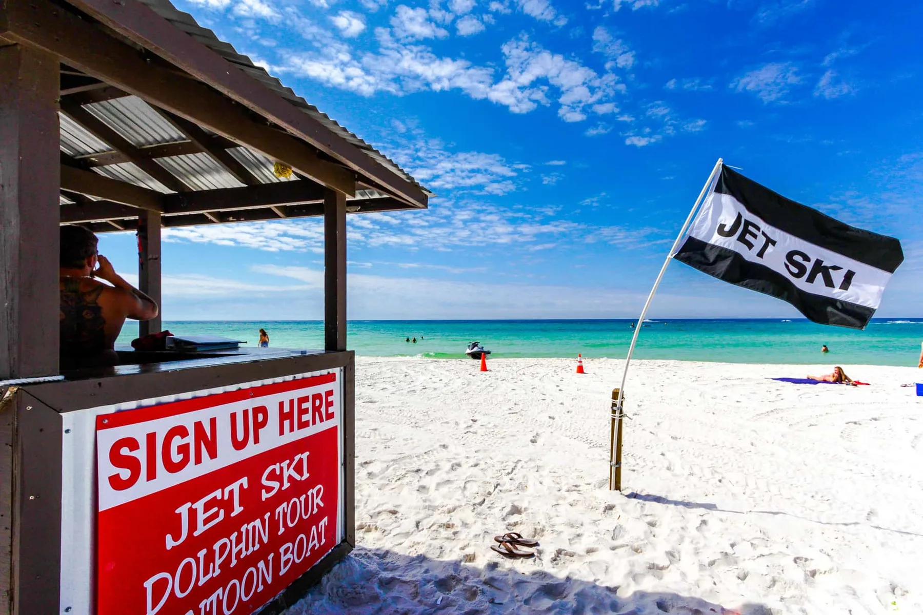A beach activity booth stands beside white sand and turquoise water.