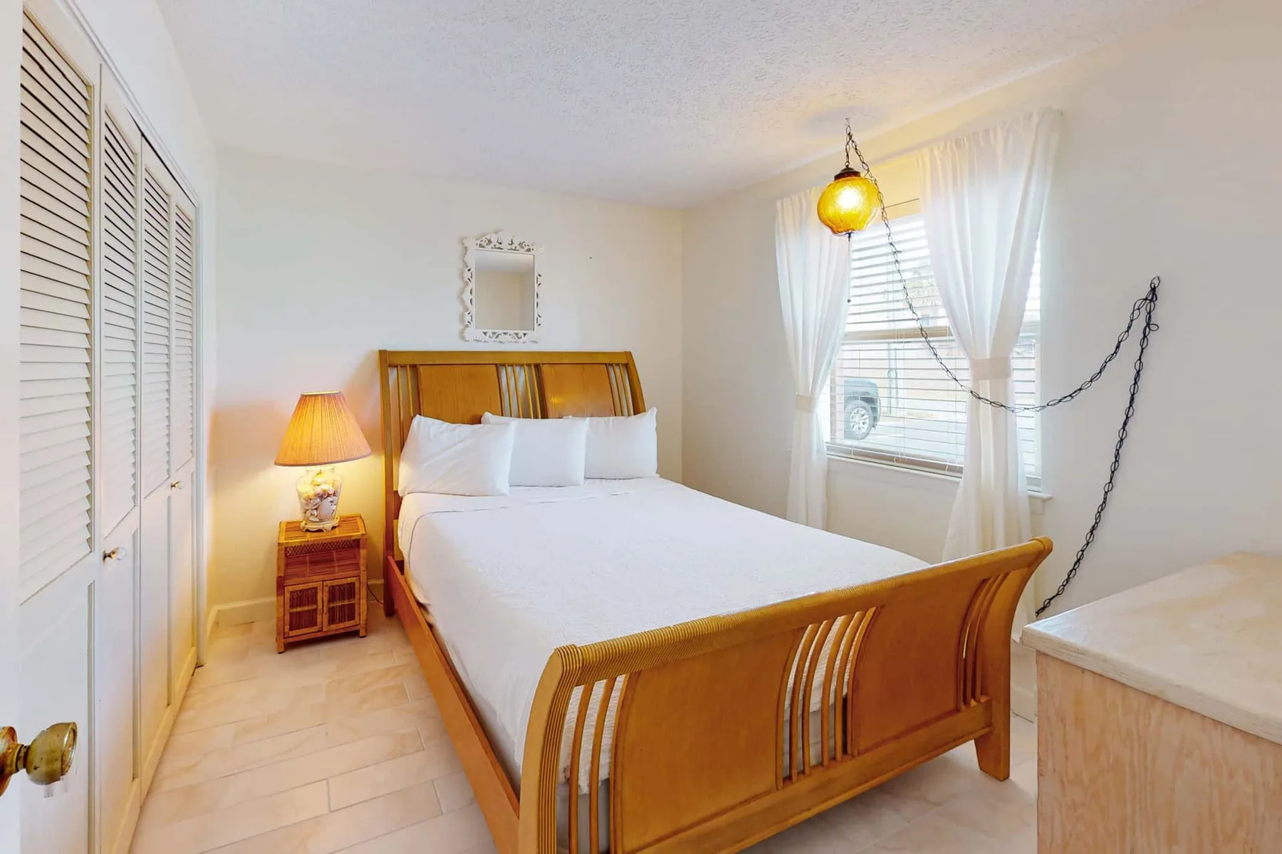 A bedroom with a wooden bed, bedside table, and a curtained window.