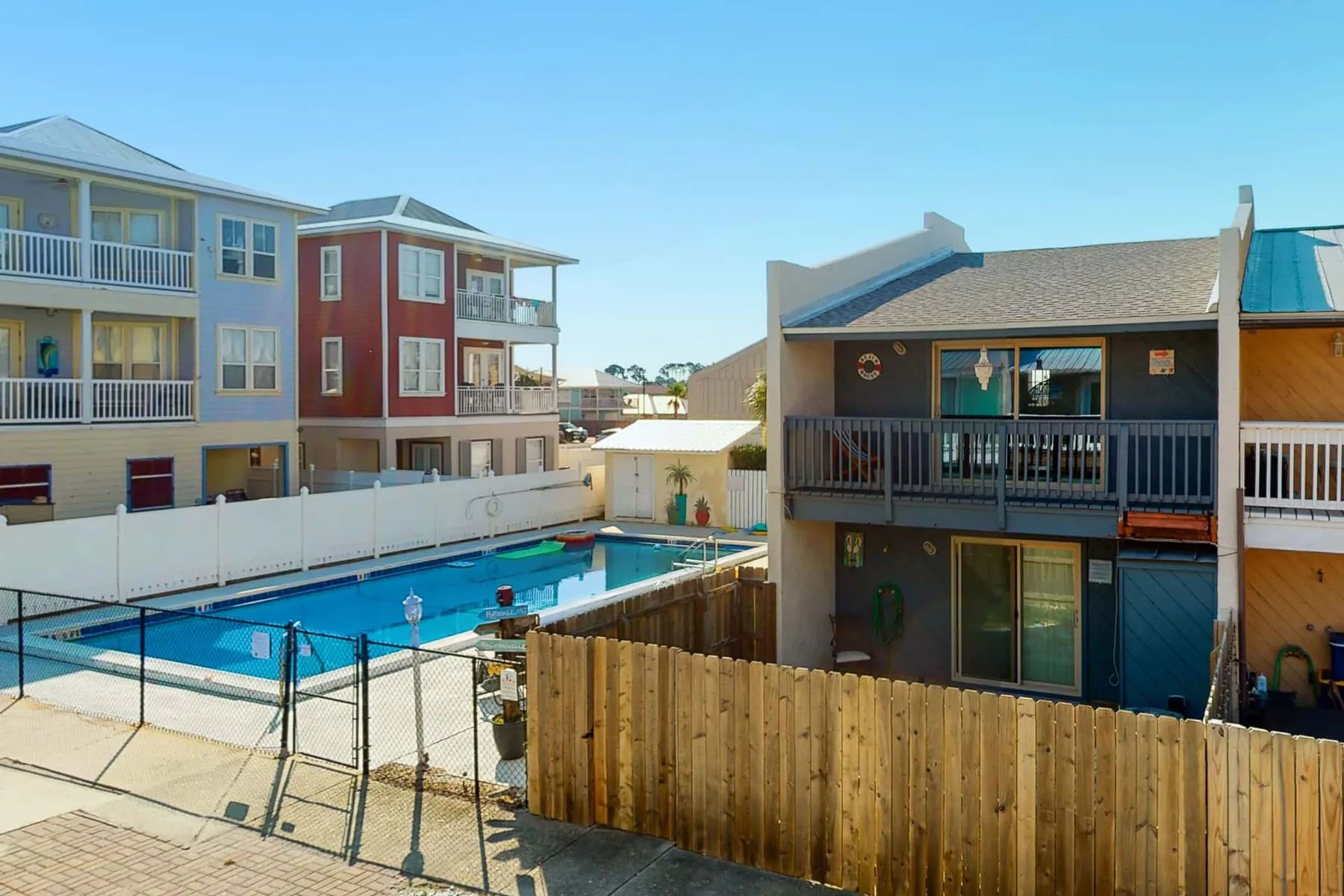 A swimming pool sits between multi-story buildings and a wooden fence.