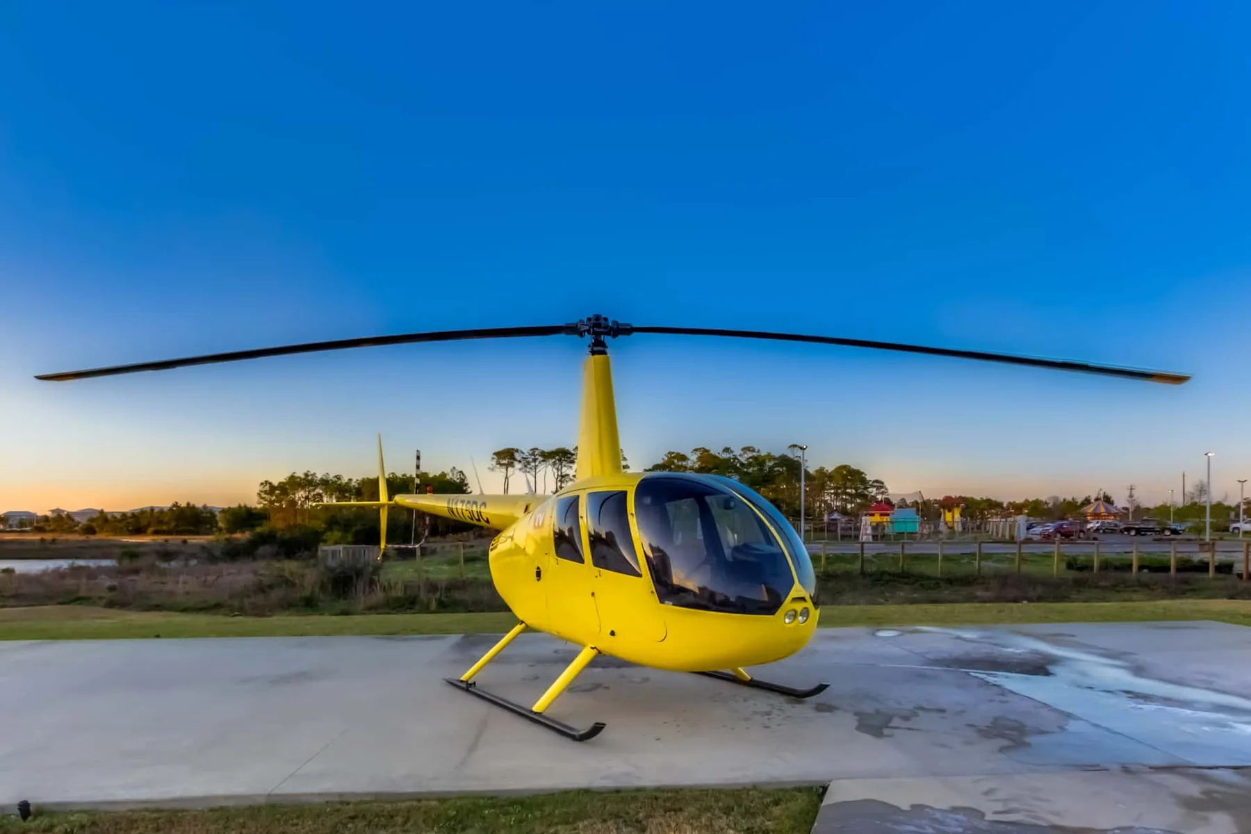 A yellow helicopter sits on a paved landing area beneath a clear blue sky.