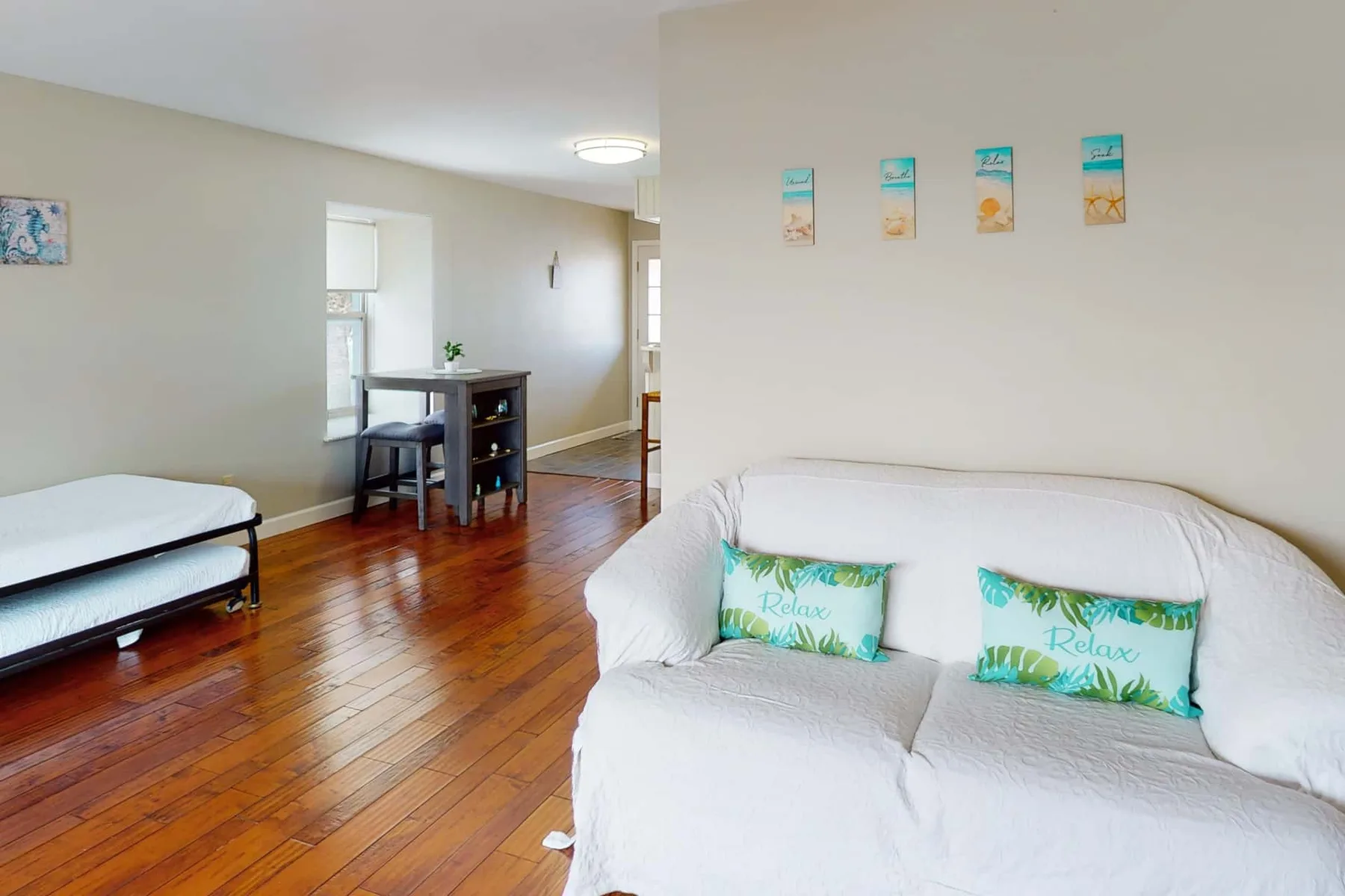 A bright living room with white seating, a small dining table, and polished wood floors.