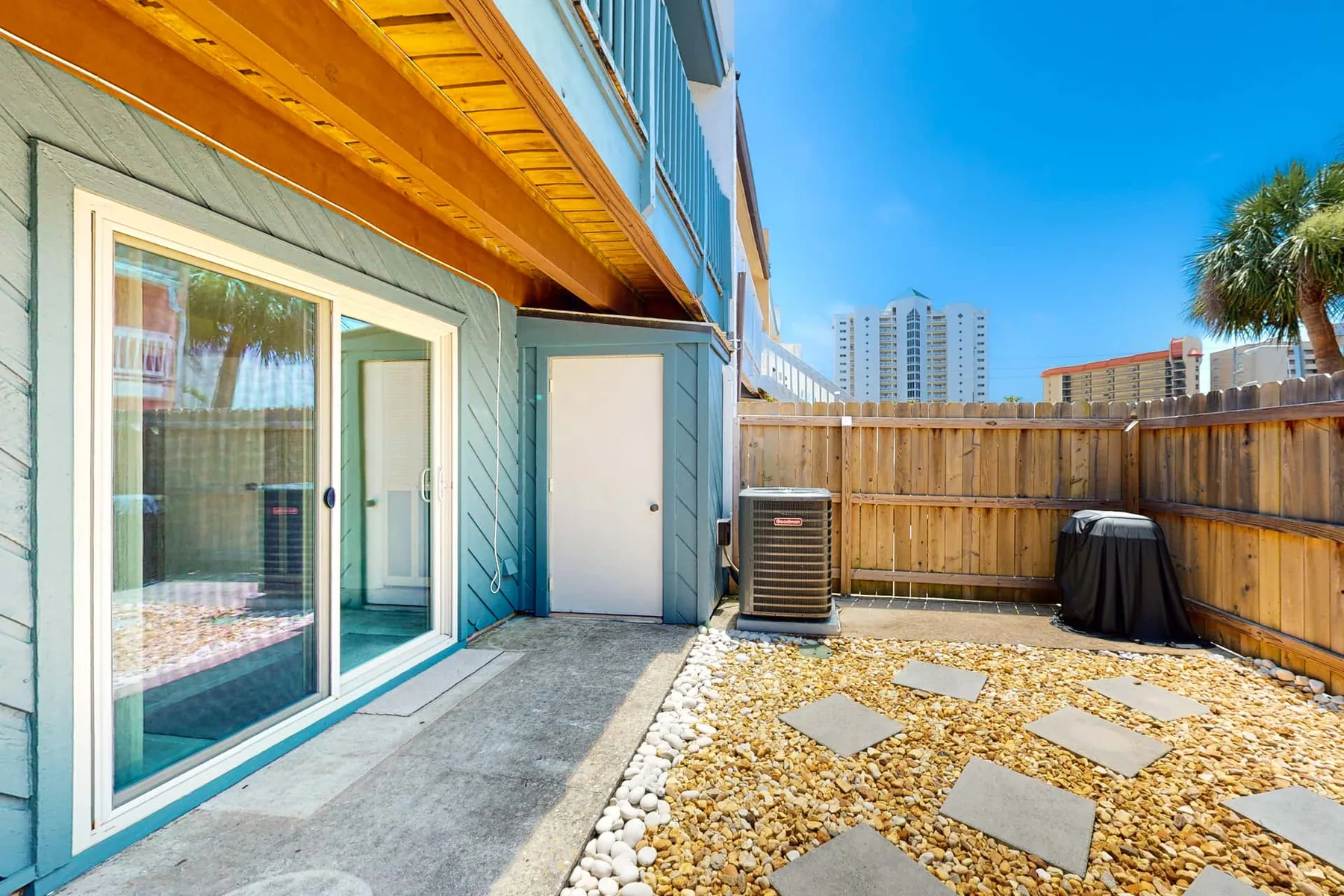 A small outdoor patio beside a building has a sliding glass door and stepping stones.