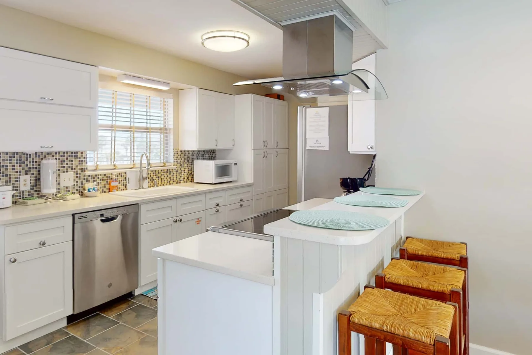 A bright kitchen with white cabinets, a central island, and bar seating.
