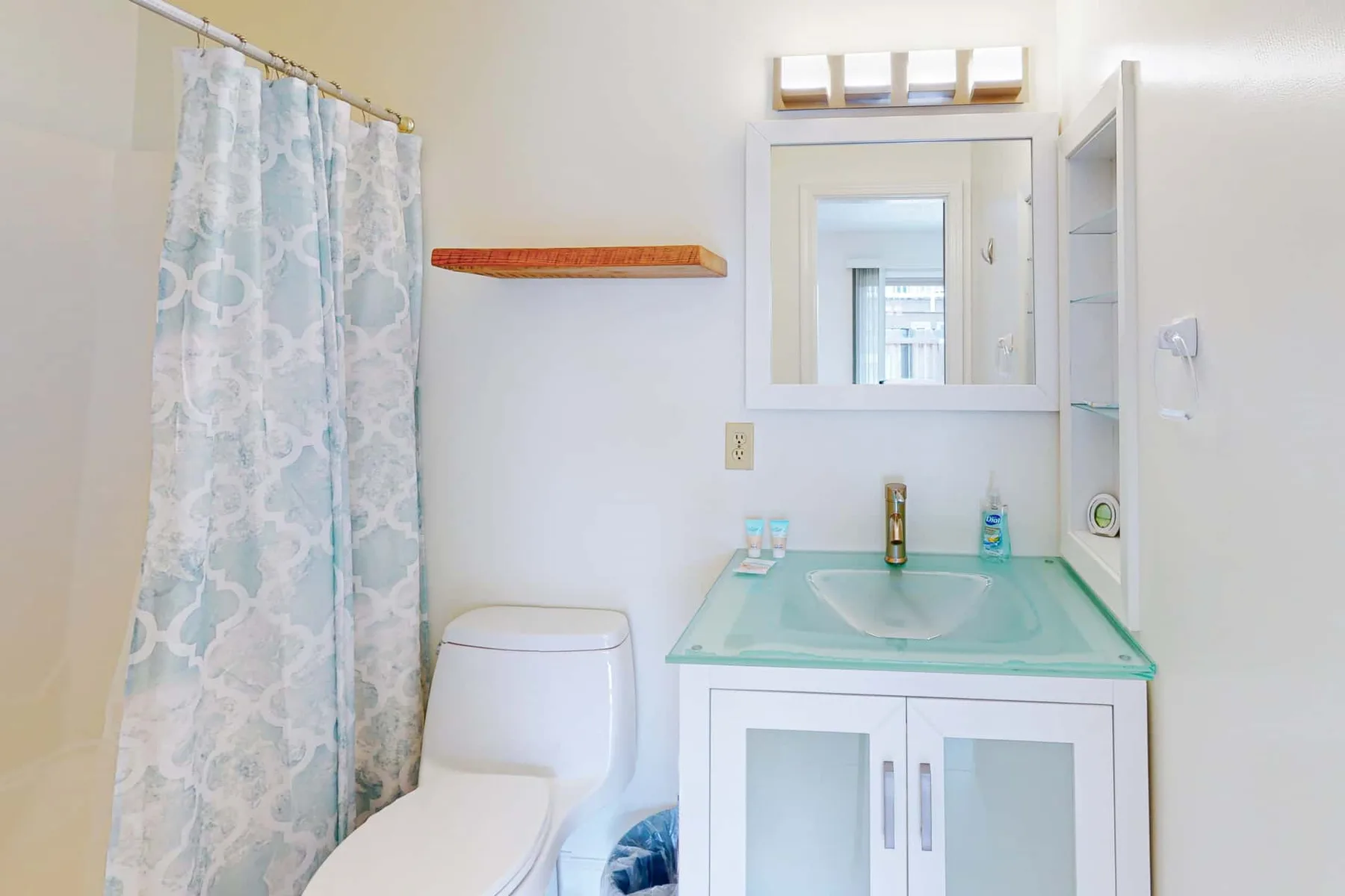 A bathroom with a sink vanity, mirror, toilet, and shower curtain.