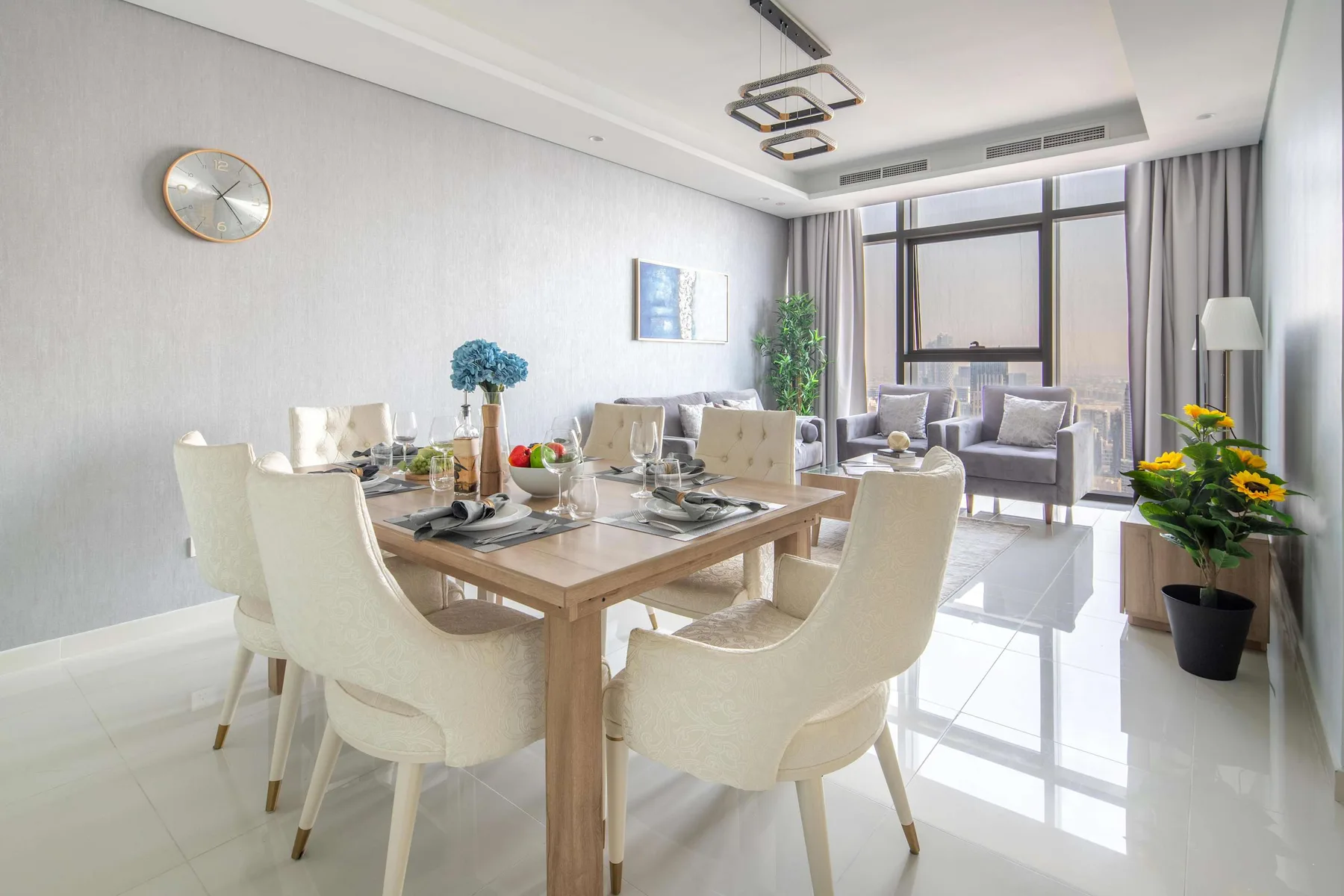 Una luminosa zona de comedor y estar con la mesa puesta y asientos junto a grandes ventanales.