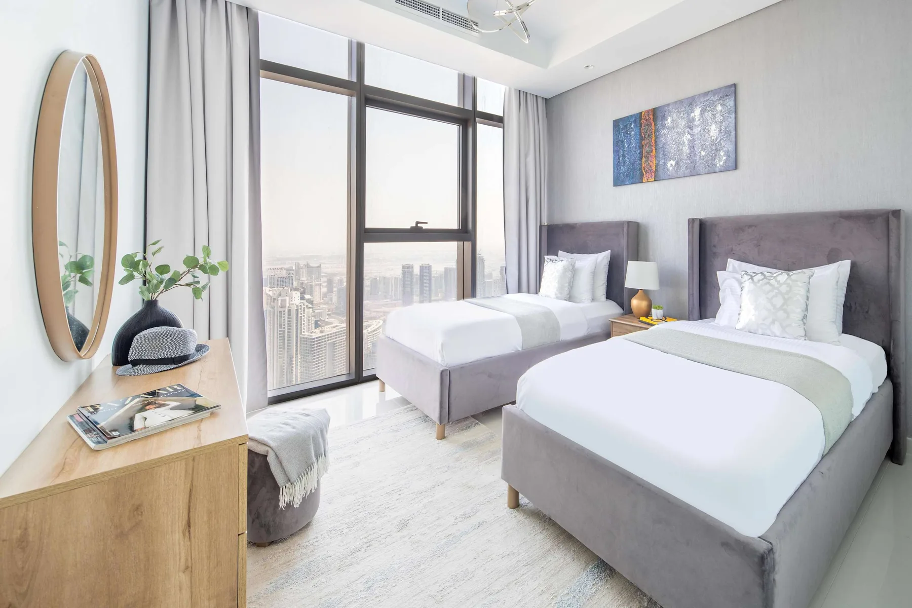 Un dormitorio luminoso con dos camas, una ventana grande y vistas a la ciudad.