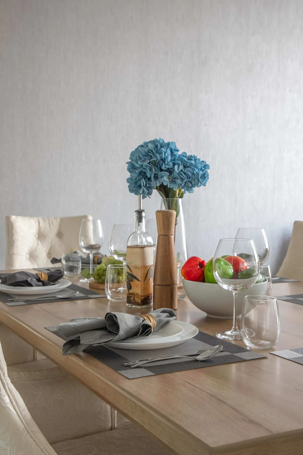 Una mesa de comedor está puesta con vajilla, cristalería y flores azules.