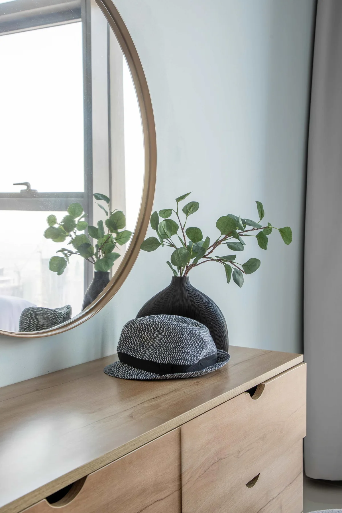 Cómoda de dormitorio con espejo redondo, un sombrero y una planta frondosa.