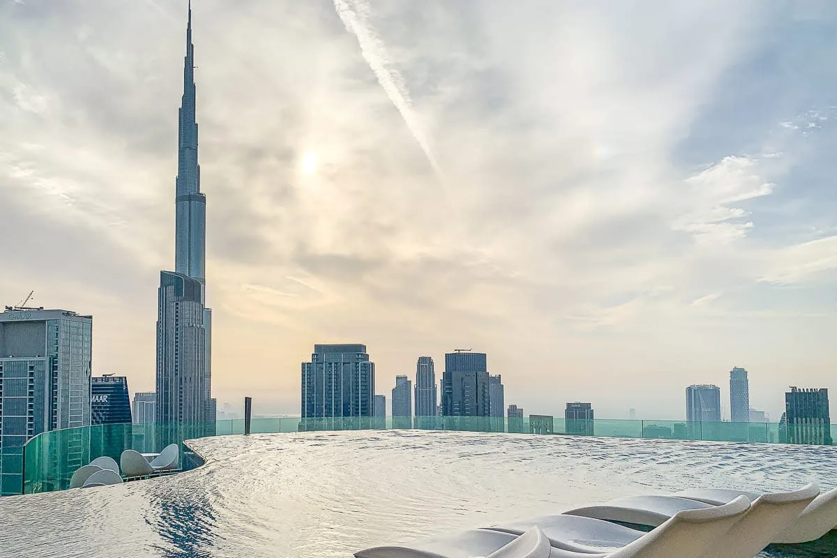 Piscina infinita en una azotea con vistas al horizonte urbano y una torre alta.