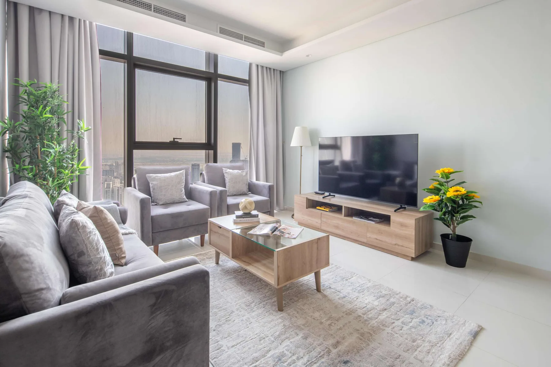 Una sala luminosa con asientos, un televisor y grandes ventanas con cortinas.
