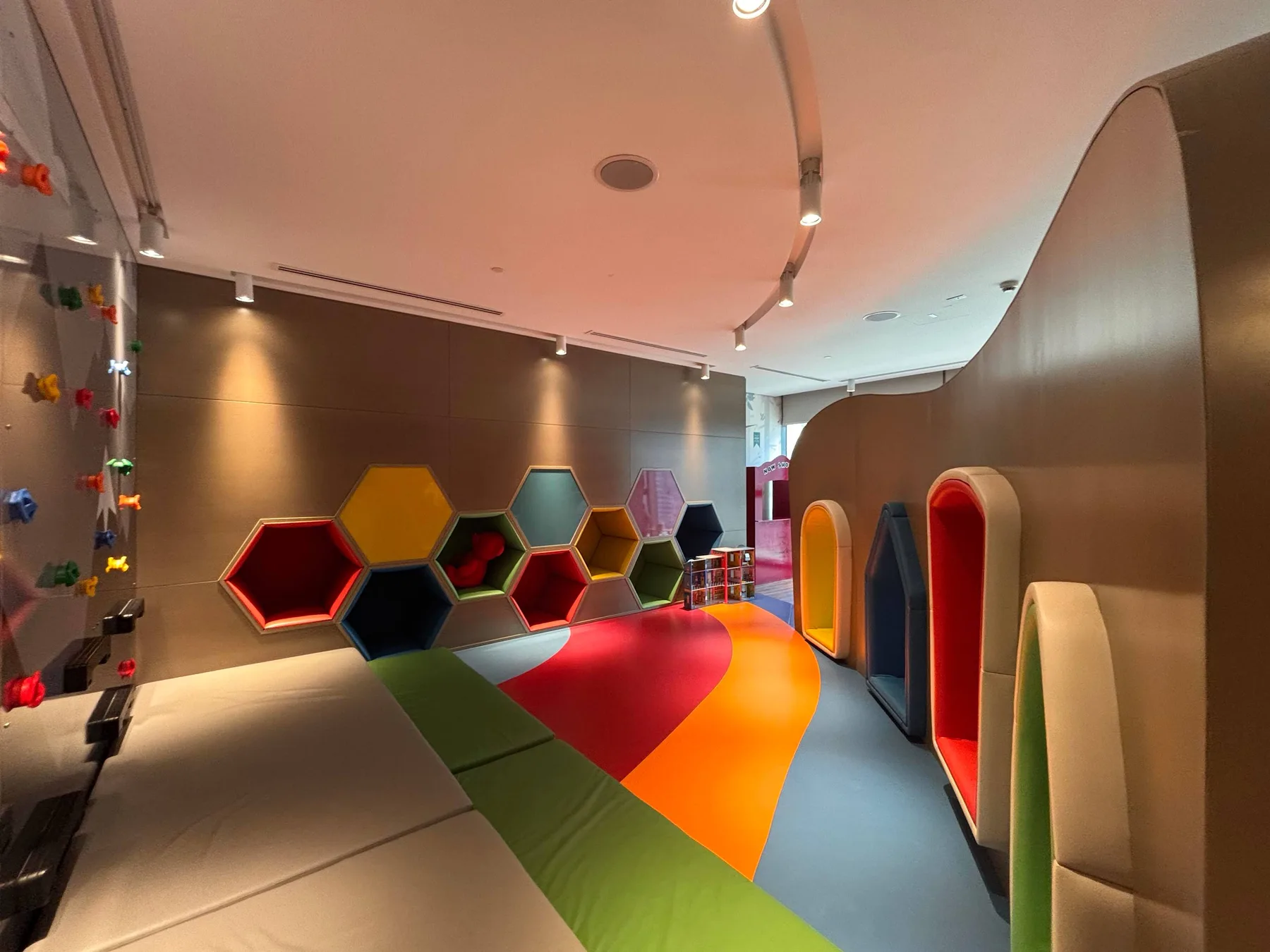 Una colorida zona de juegos interior con asientos acolchados y un suelo multicolor sinuoso.
