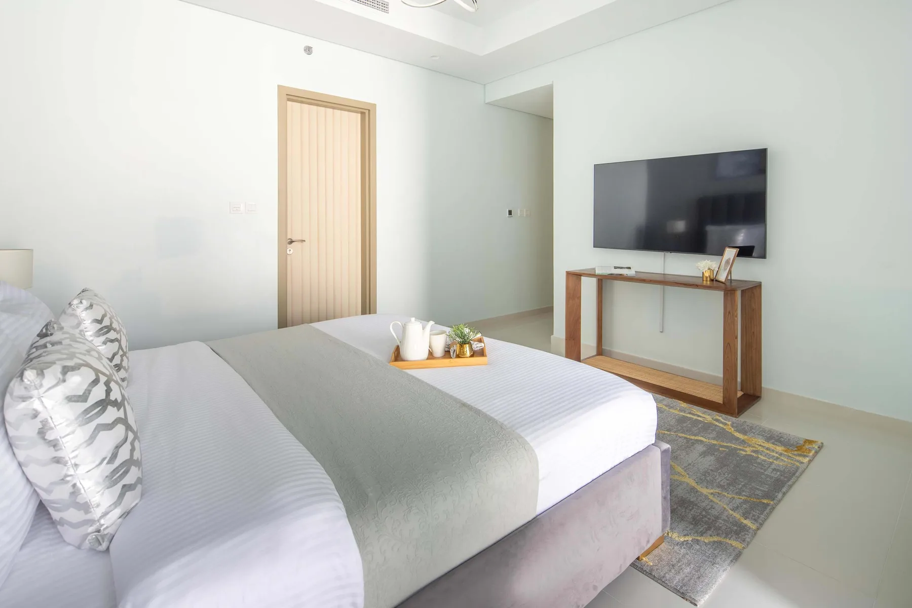 Un dormitorio luminoso con una cama tendida y un televisor sobre una consola.