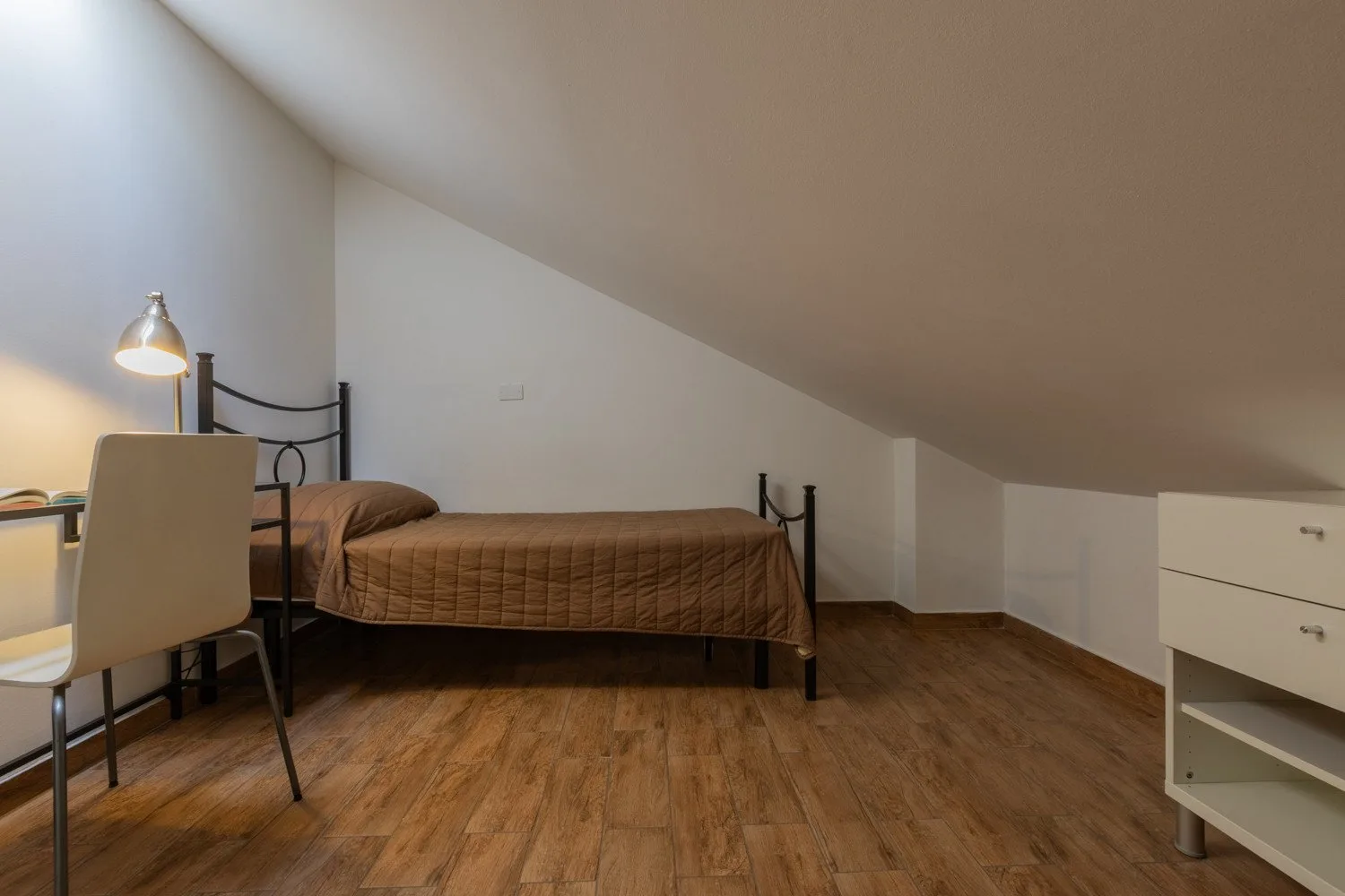 Dormitorio con cama, escritorio y techo inclinado.