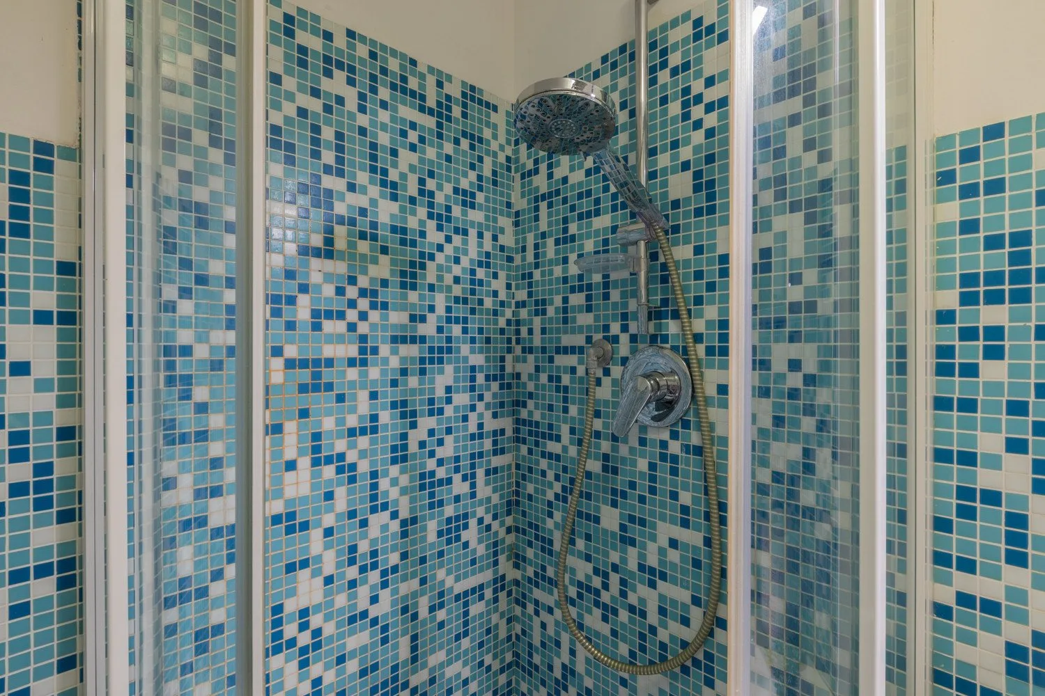Una ducha con paredes de mosaico azul y blanco y una ducha de mano.