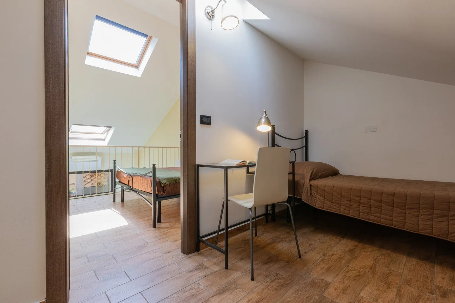 Un dormitorio tipo loft con escritorio, silla y cama bajo un techo inclinado.