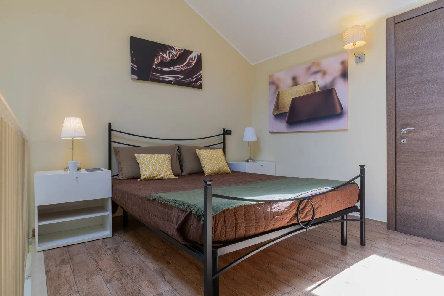 A bedroom with a double bed, bedside tables, and wall art.